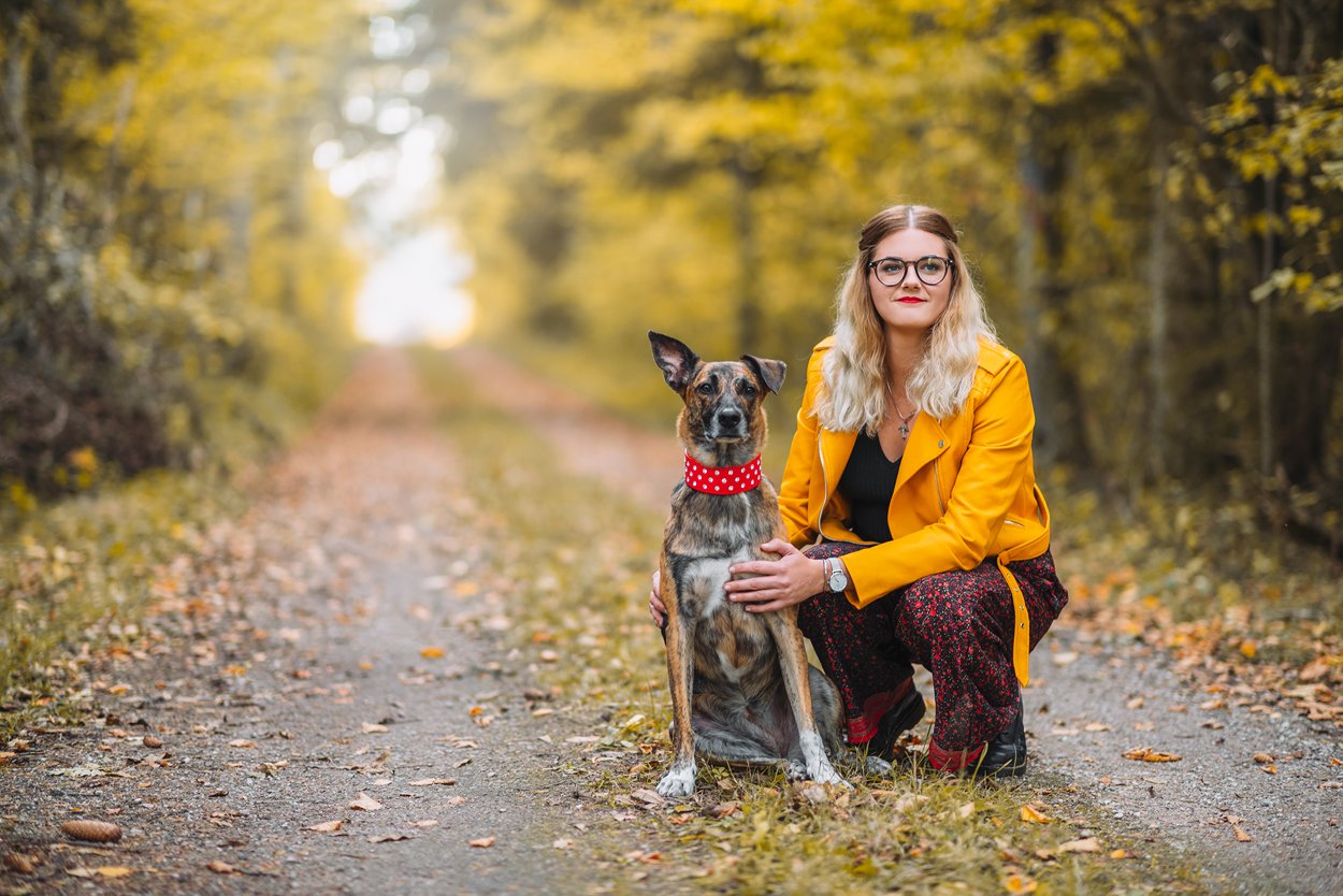 Woman crouching beside her dog in a colorful autumn forest during an outdoor photo session.