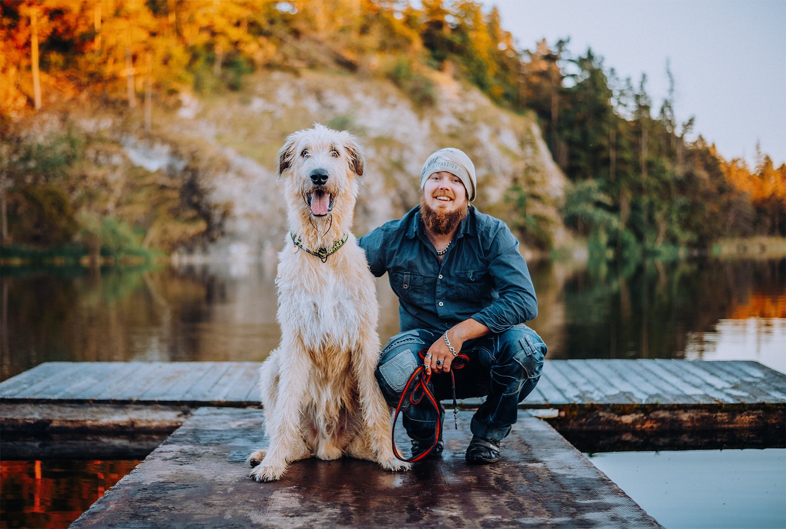 Man sitting on a dock with his large dog during an outdoor photo session by the lake in autumn light.