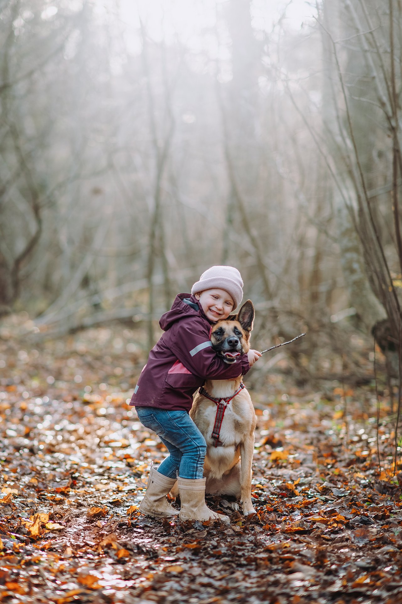 miling girl in a purple coat hugging her dog on a forest path covered with autumn leaves.
