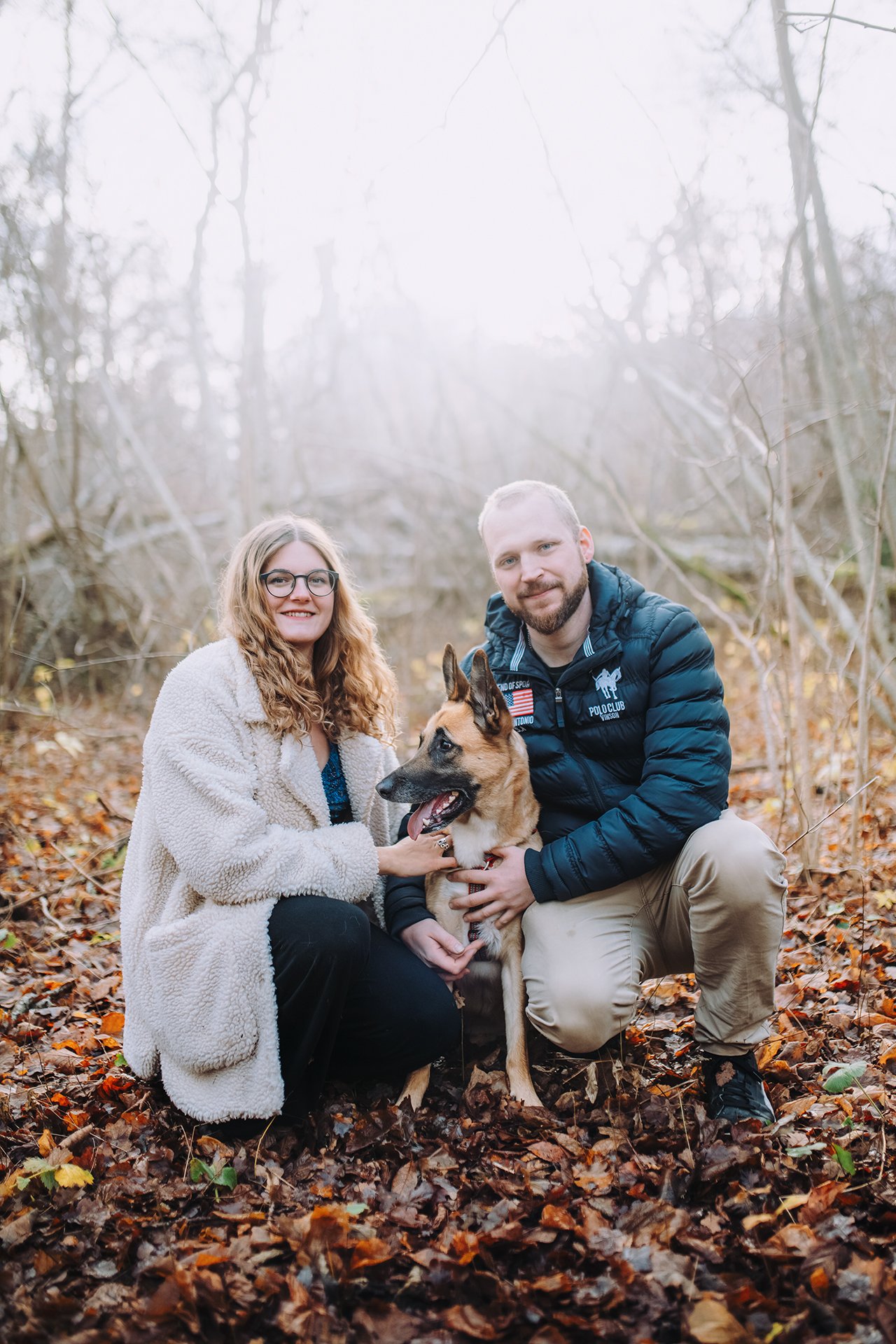Couple sitting close together with their dog during an outdoor autumn photo session at sunset.