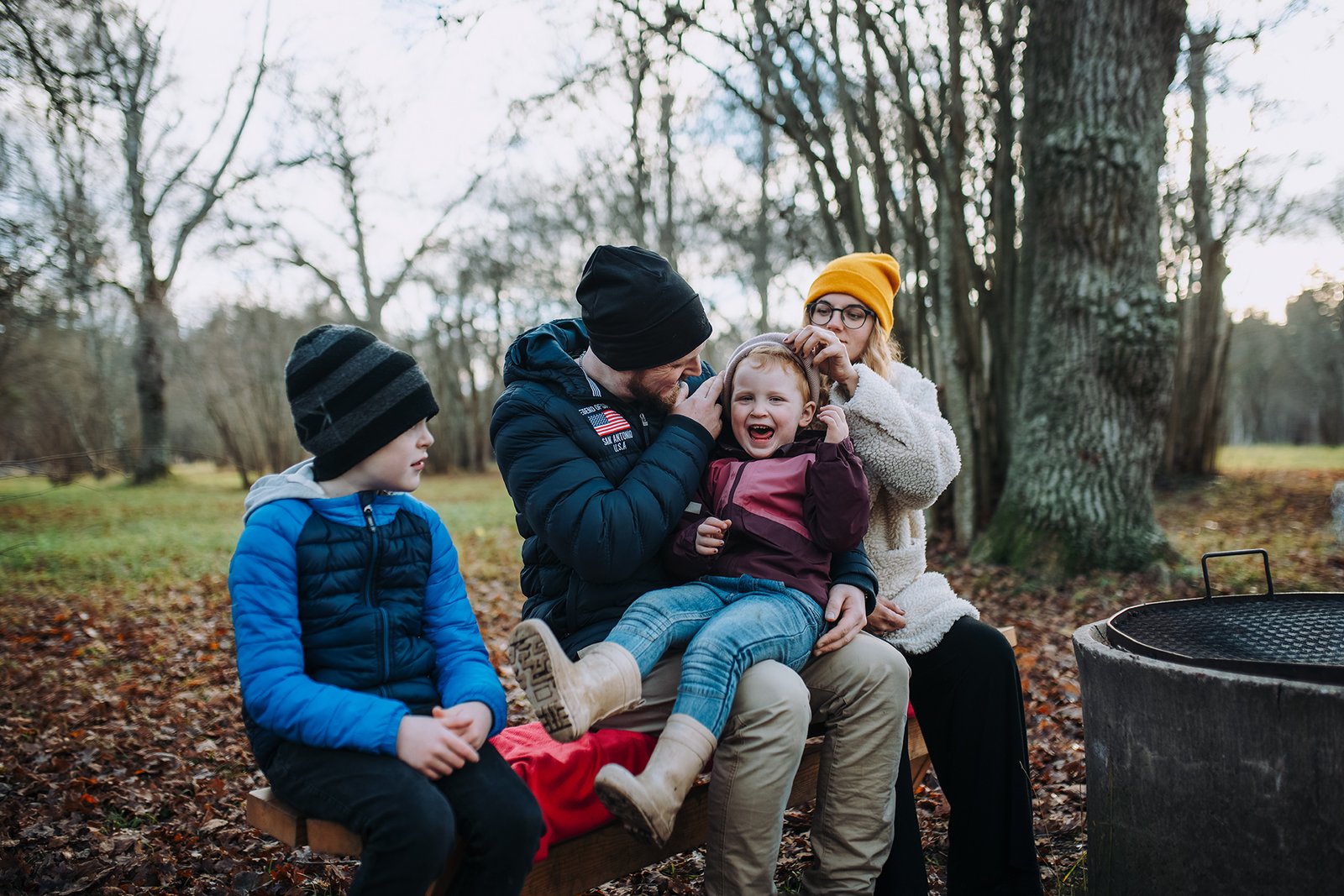Familj sitter tillsammans vid eldstad i skogen