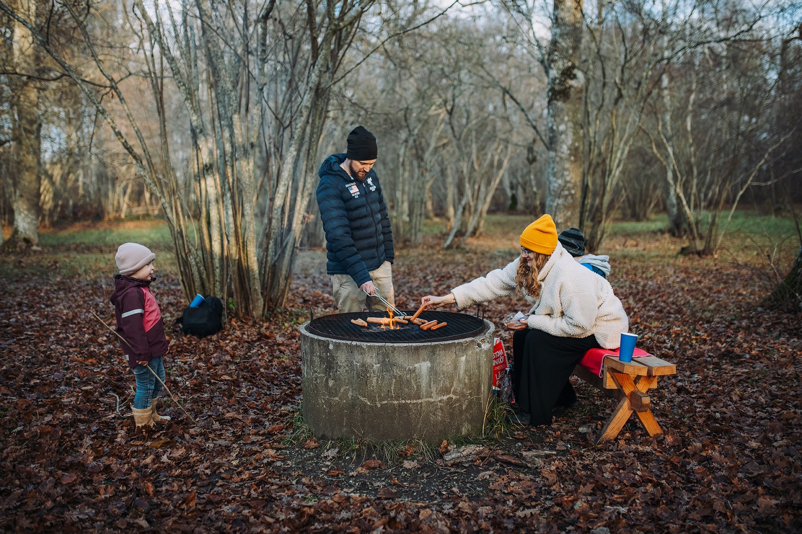 Familj grillar korv vid eldstad i skogen