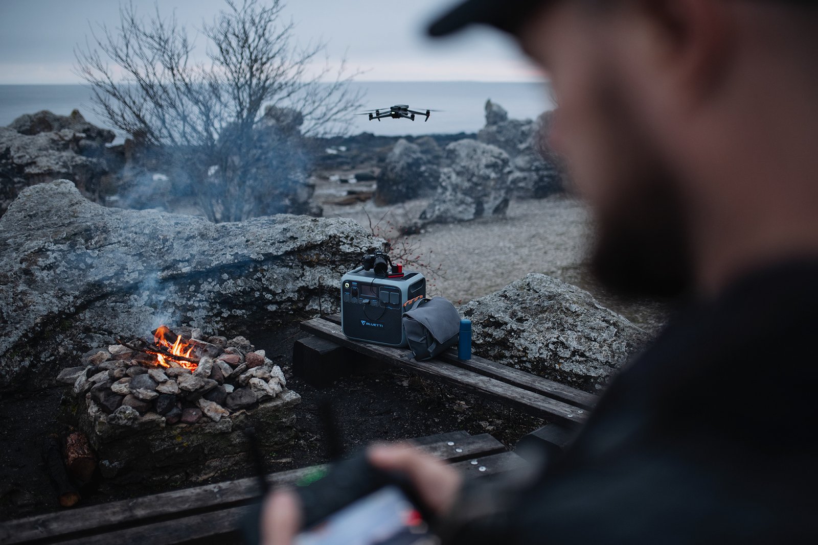 Drönartjänster Drönare lyfter vid stenstrand på Gotland, med lägereld och pilot i förgrunden.