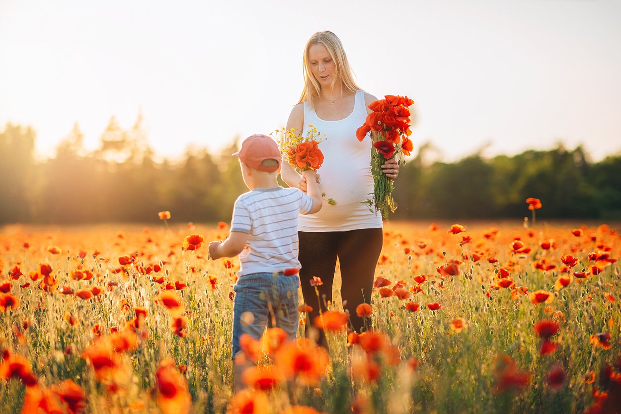 Linda står i ett vallmofält och håller blommor medan sonen Axel räcker henne en bukett i kvällsljus.