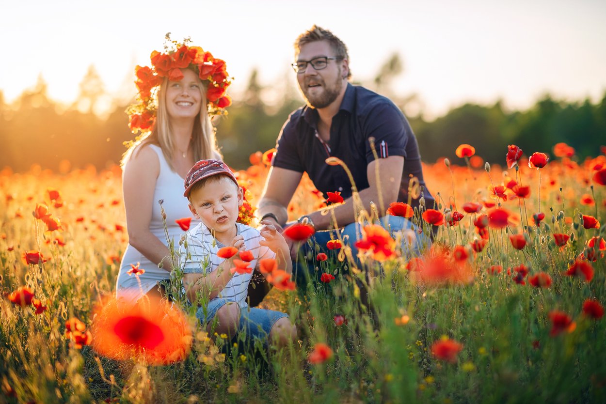 Familjen Linda, Tobbe och Axel sitter i ett blommande vallmofält i kvällssol.