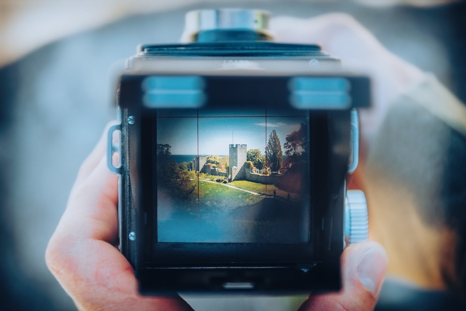 Händer håller en Yashica mellanformatskamera med Visby ringmur synlig genom sökaren.